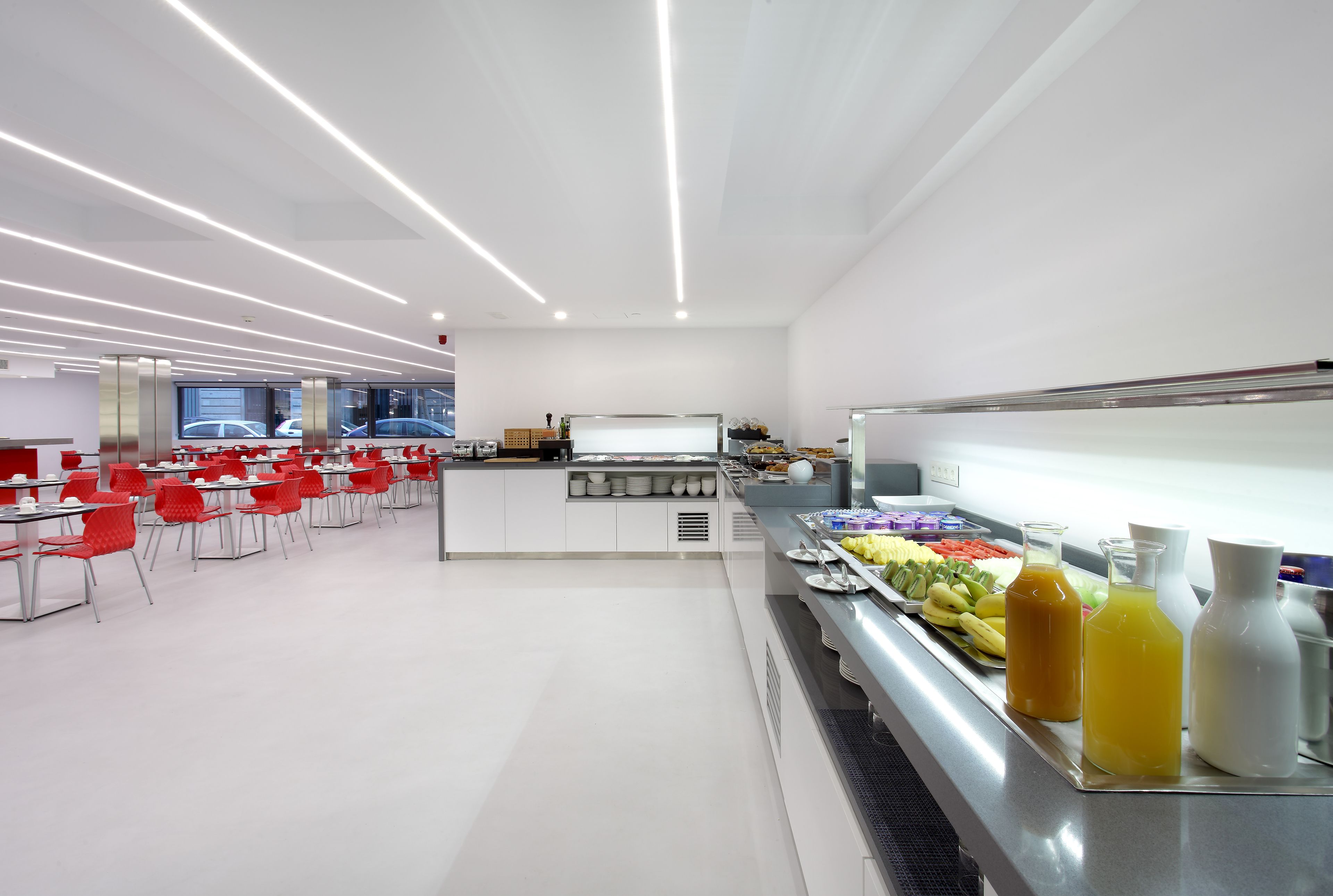 Une cafétéria moderne aux murs blancs, aux chaises rouges et dotée d’un comptoir buffet proposant une variété de plats et de boissons.