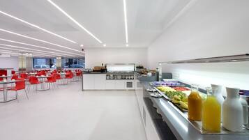 Une cafétéria moderne aux murs blancs, aux chaises rouges et dotée d’un comptoir buffet proposant une variété de plats et de boissons.