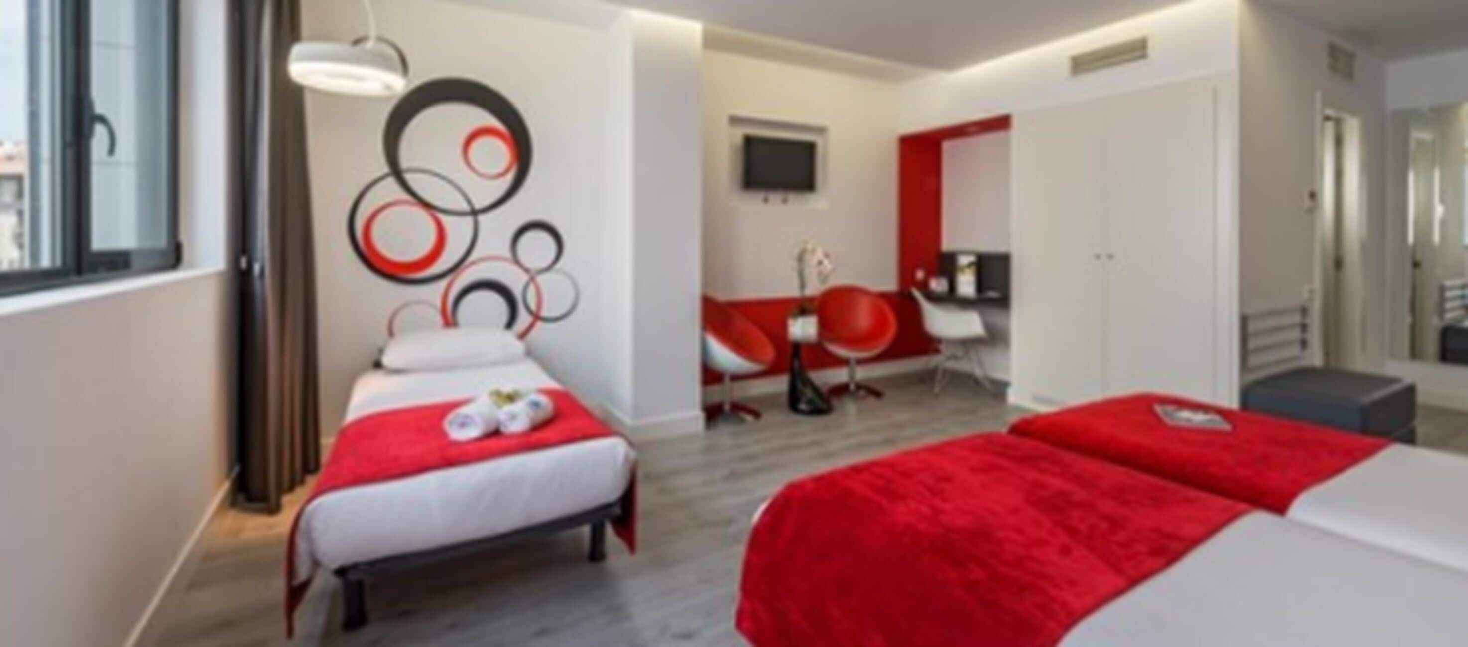 Ein Hotelzimmer mit zwei Betten, einem Fernseher, einem Schreibtisch und einem Sessel.