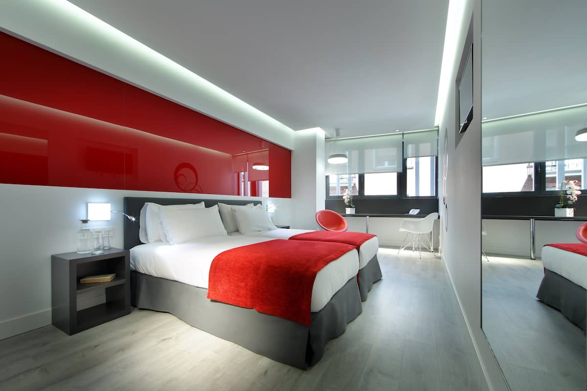 A modern bedroom with a large bed, bedside tables, a desk, and a chair.