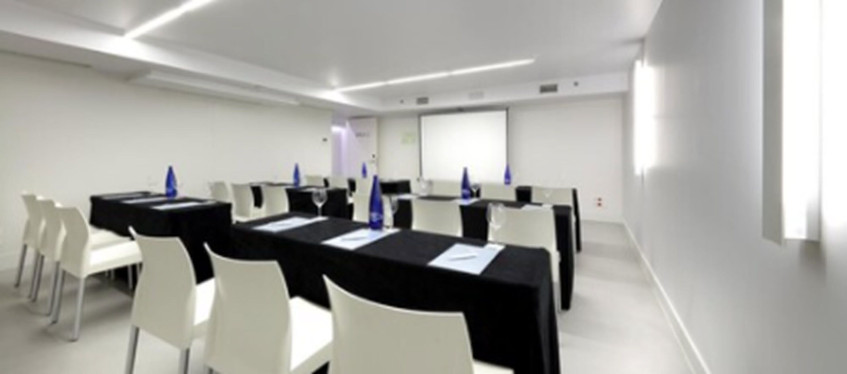 Une salle de conférence avec des chaises et des tables blanches, un écran de projection et un tableau blanc.