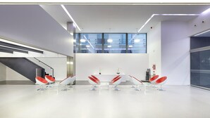 Un moderno salón de conferencias con una mesa blanca, sillas rojas y un amplio ventanal.