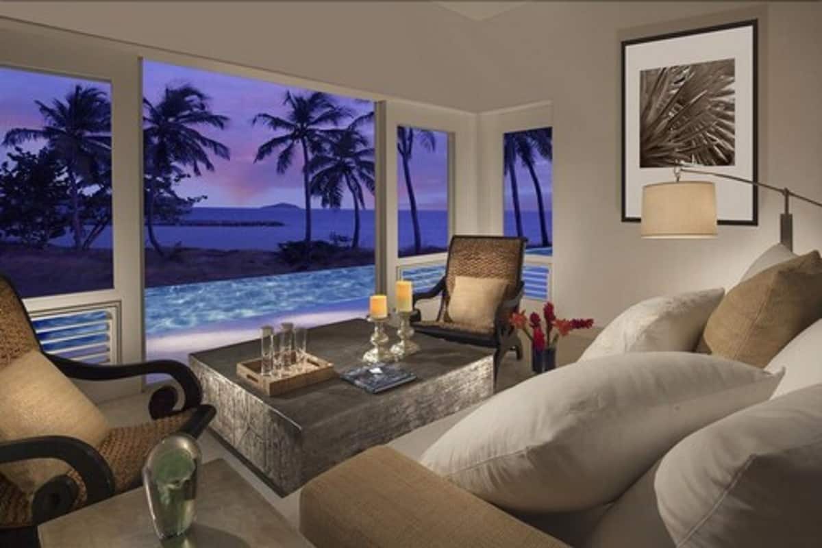 A living room with a view of a beach at sunset, a coffee table with candles, and a framed picture on the wall.