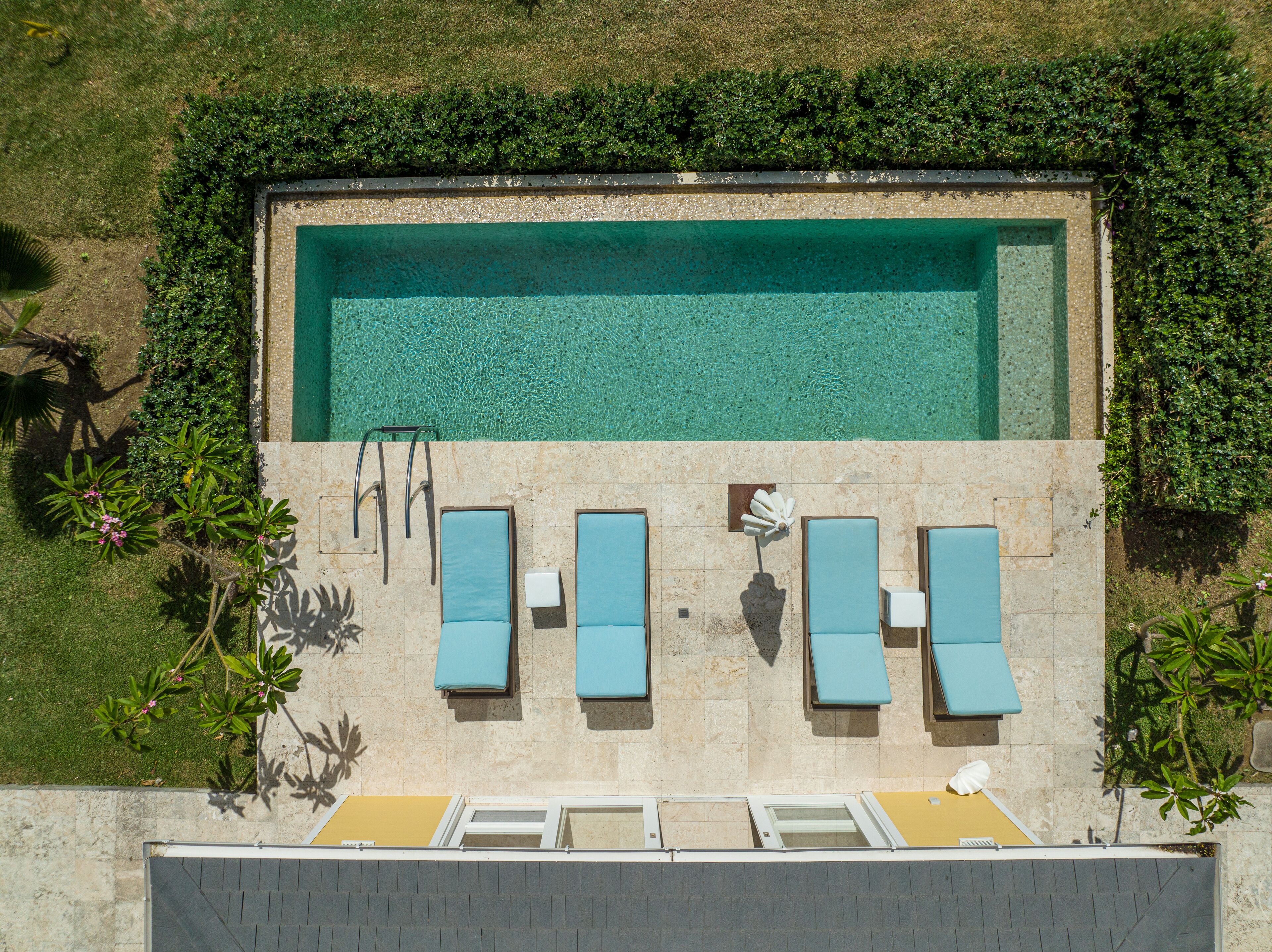 Eine Vogelperspektive auf einen rechteckigen Pool mit klarem Wasser, umgeben von einer Steinmauer und einer Reihe blauer Liegestühle.