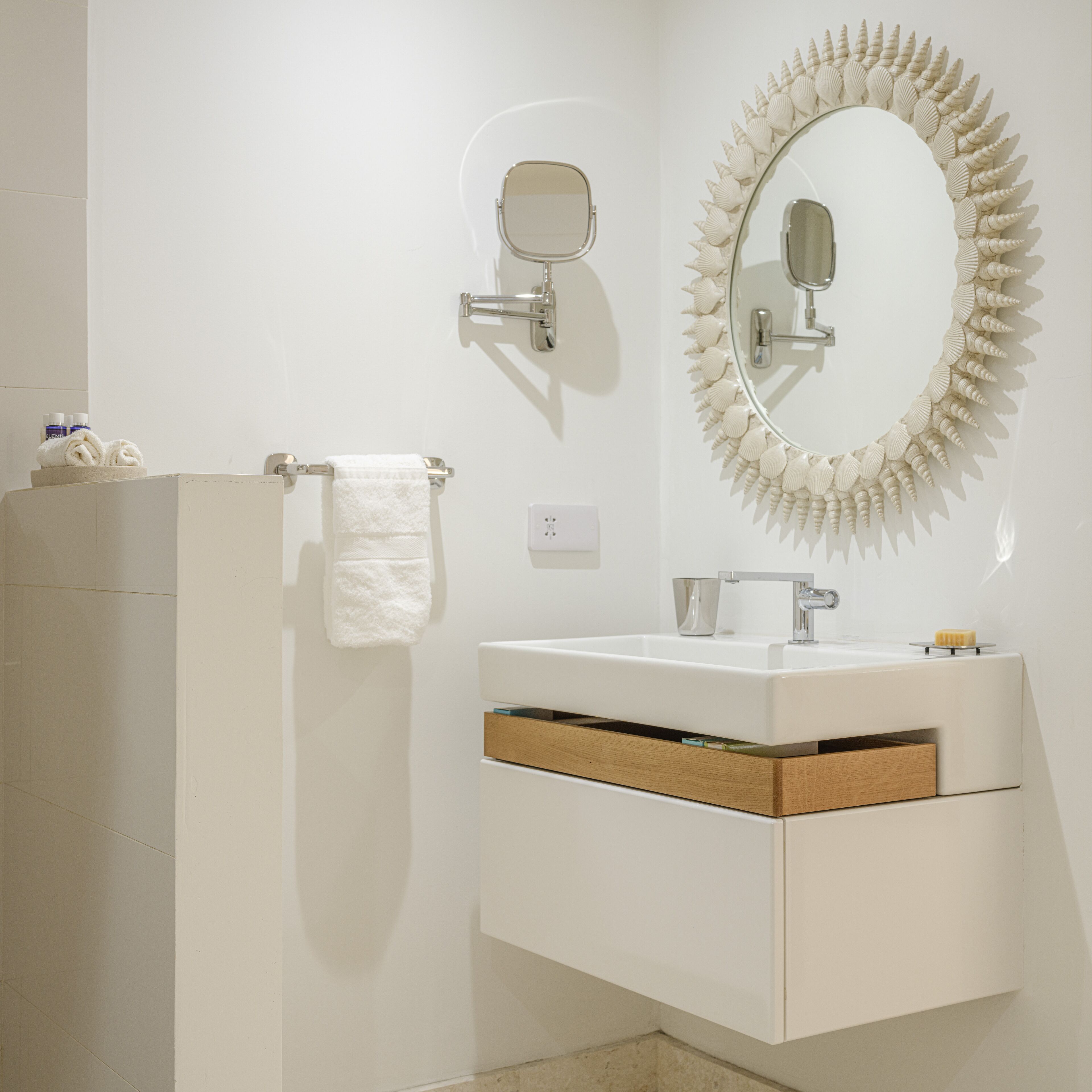 Une salle de bain moderne avec un meuble-lavabo blanc, un miroir rond orné d’un motif en forme de coquillage et une serviette suspendue à un porte-serviettes.