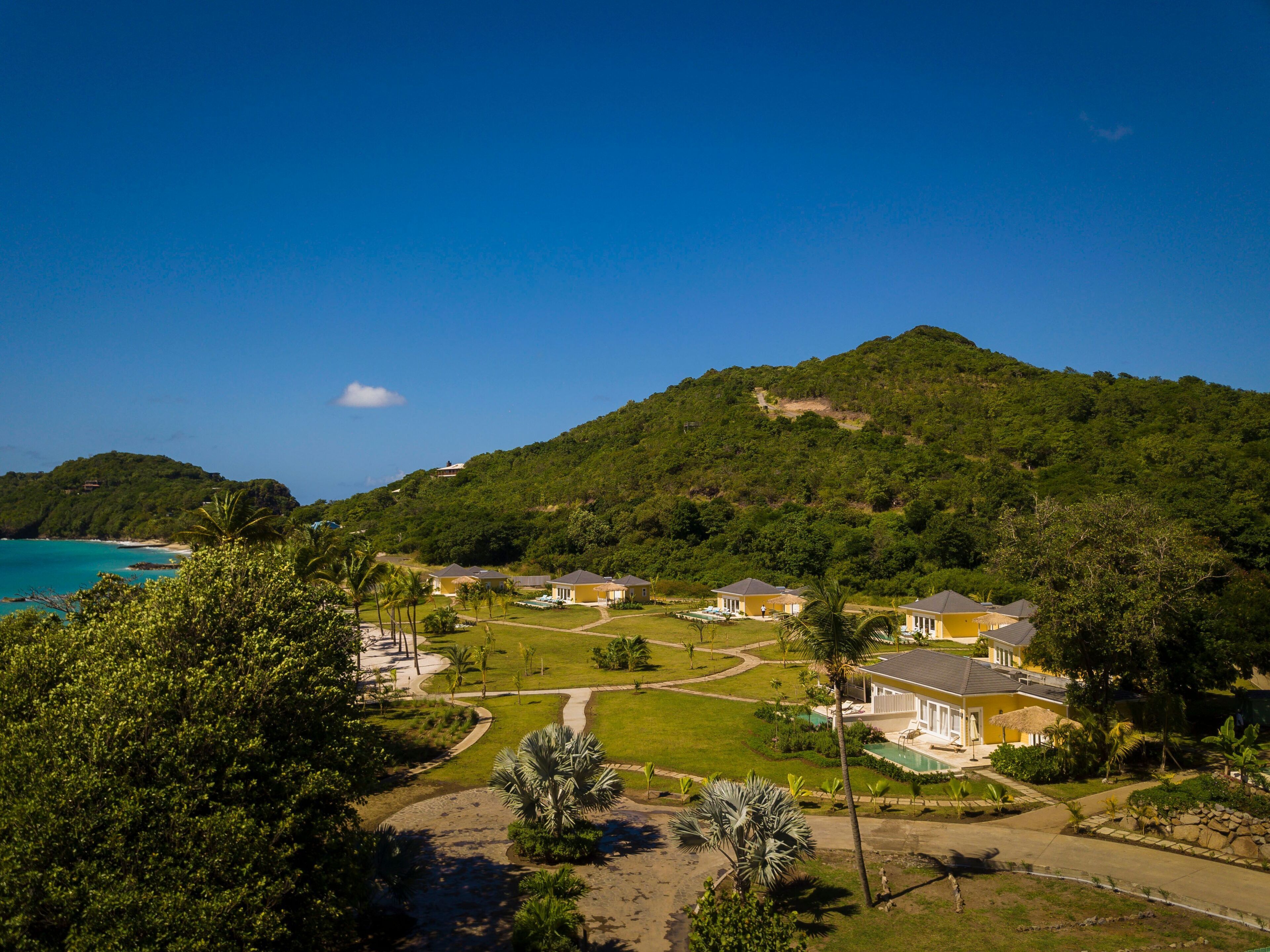 A resort with multiple buildings, a swimming pool, and a view of the ocean and a mountain.
