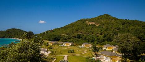 A resort with multiple buildings, a swimming pool, and a view of the ocean and a mountain.