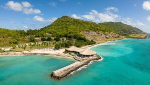 Une station balnéaire dotée d’une plage, d’une structure à toit de chaume et d’une jetée s’avançant dans des eaux turquoise.