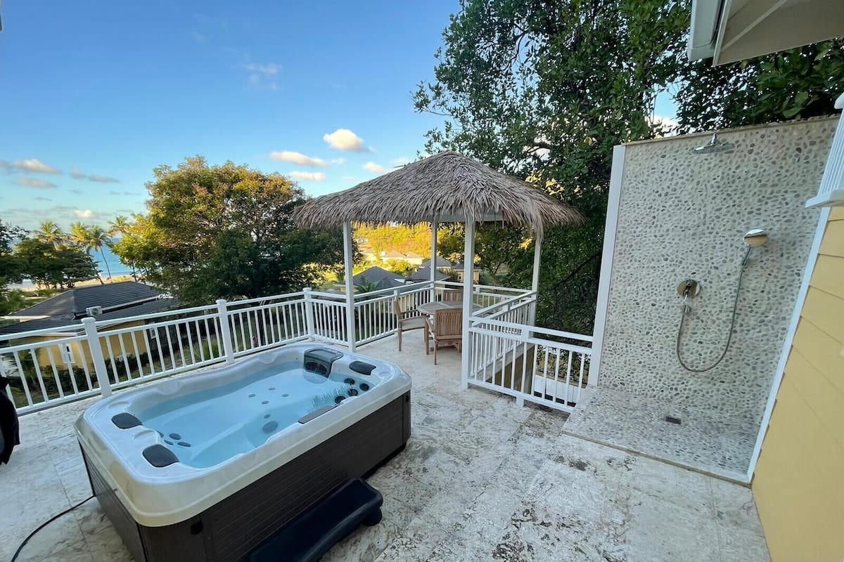 A hot tub and a shower area with a view of the beach and trees.