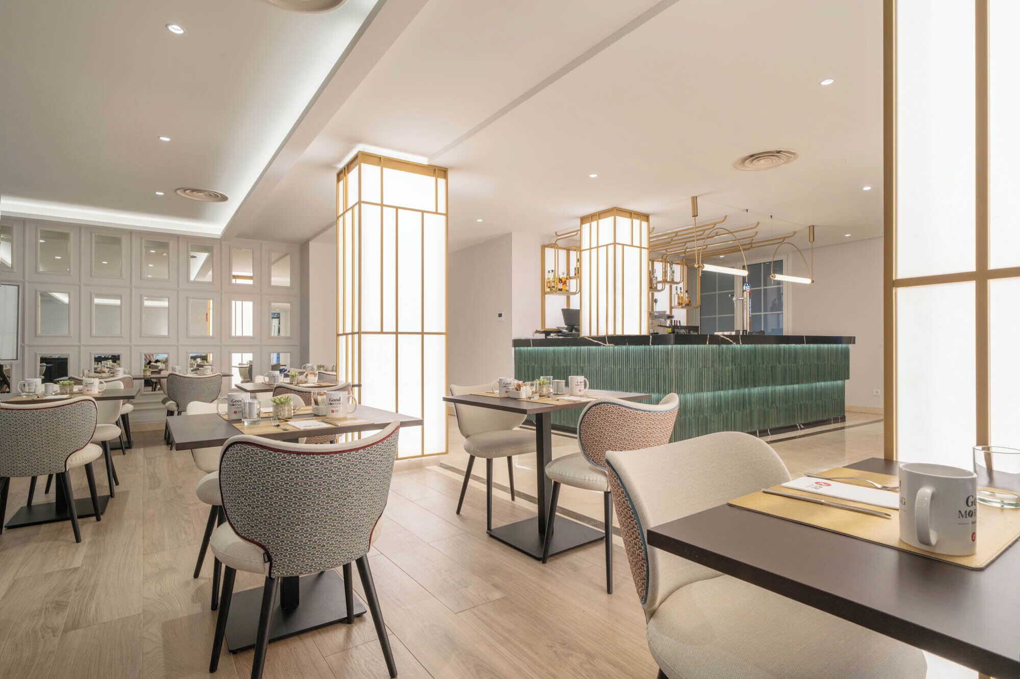 A modern restaurant with multiple dining tables and chairs, a green booth area, and a bar counter.