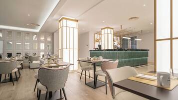 A modern restaurant with multiple dining tables and chairs, a green booth area, and a bar counter.