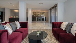 Een ruime lobby met twee rode banken, een zwarte salontafel en een receptiebalie met een behang.'
