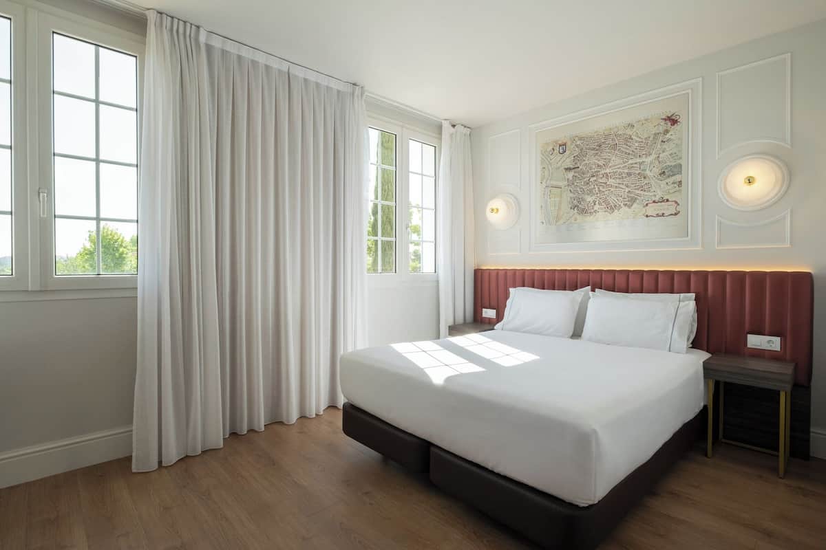 Habitación de hotel con una cama grande, una mesita de noche, un mapa en la pared y una ventana con cortinas.