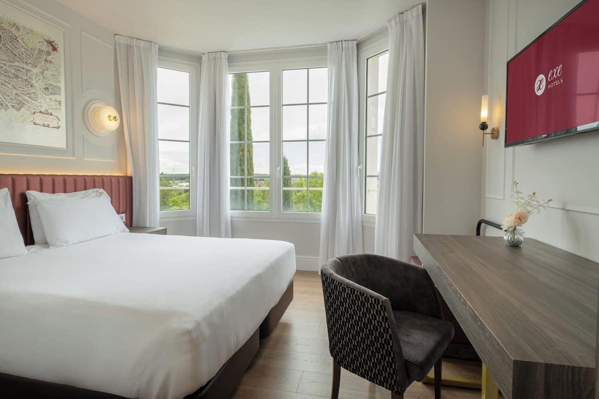 Une chambre d’hôtel avec un grand lit, un bureau, une chaise et un téléviseur fixé au mur.