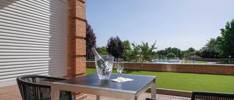 Un patio al aire libre con una mesa y sillas, una chimenea de ladrillo y vistas a una piscina y zonas verdes.