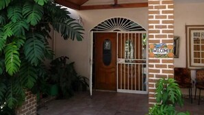 A covered entrance with a wooden roof, a brick pillar with a 'WELCOME' sign, and a tiled floor. - Star House (Port-au-Prince)