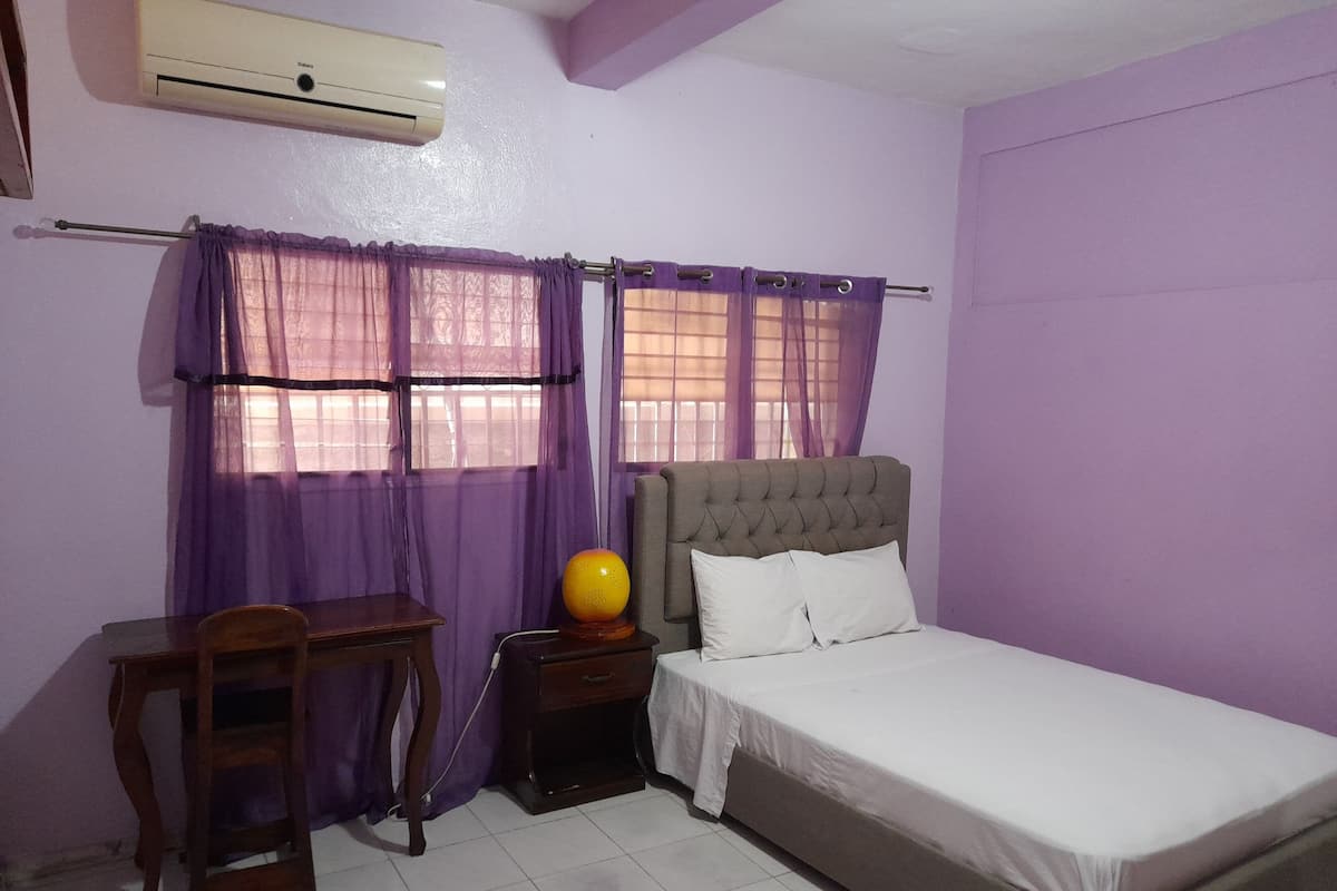 A bedroom with a bed, a nightstand, a desk, and purple curtains.