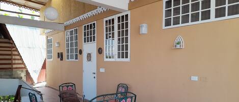 Un patio cubierto con una mesa y dos sillas, una puerta y un ventanal con marco decorativo.