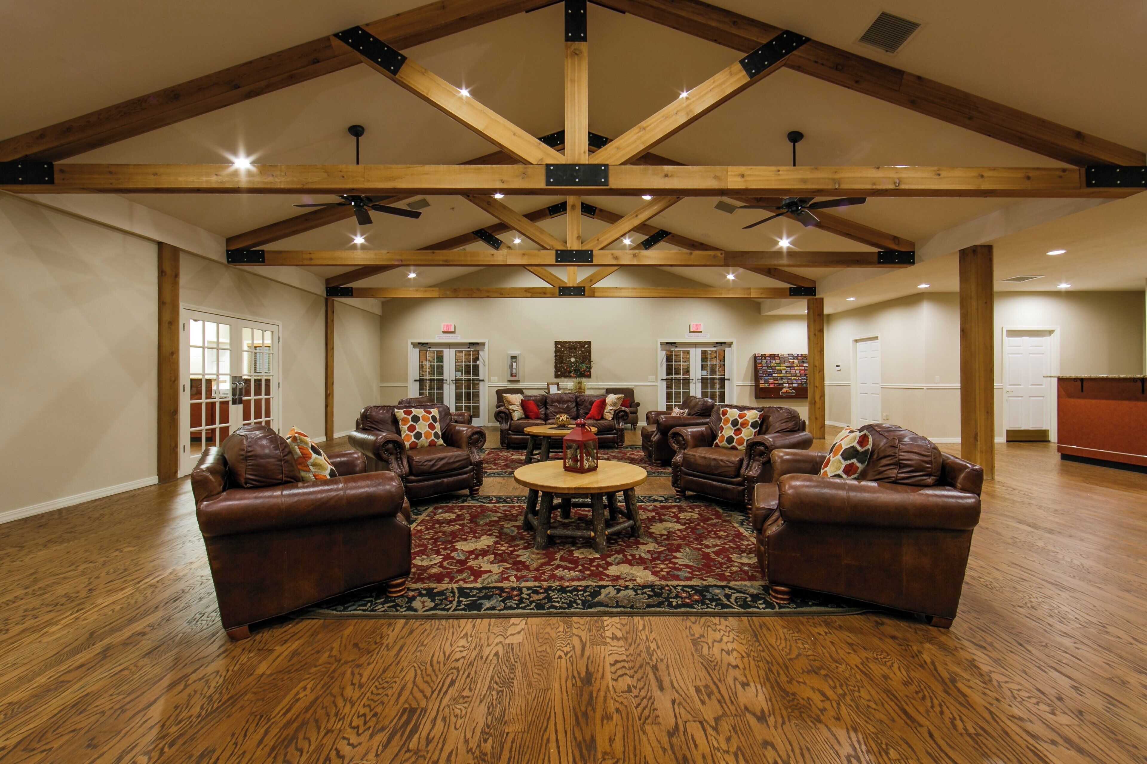 A spacious living room with leather sofas, a wooden floor, and a high ceiling with exposed beams.