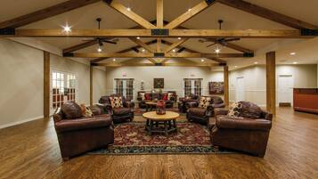 A spacious living room with leather sofas, a wooden floor, and a high ceiling with exposed beams.