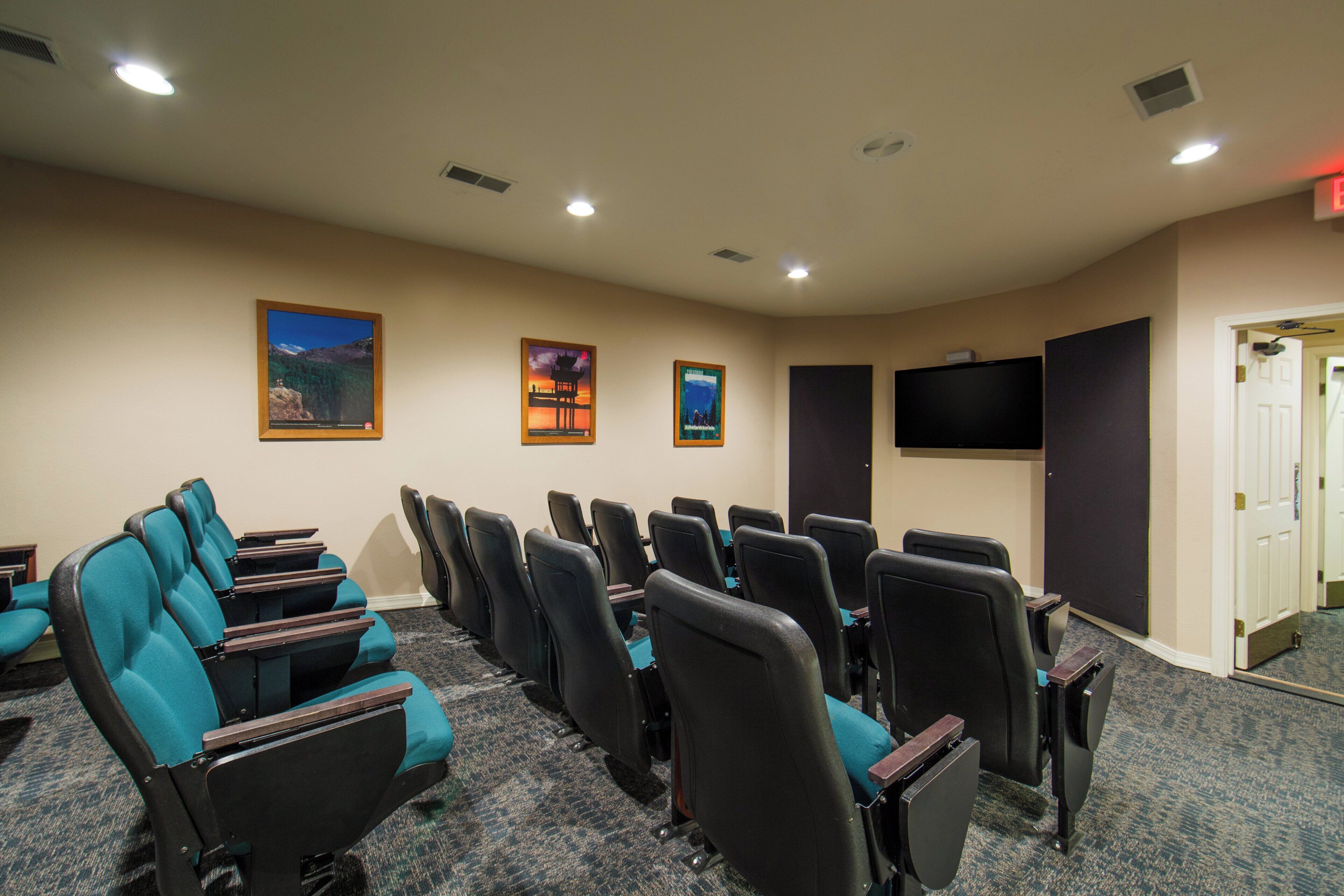 A conference room with rows of chairs, a large screen, and a door leading to another room.