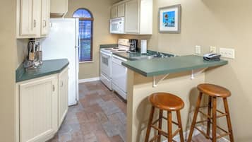 A kitchen with a built-in island, bar stools, a refrigerator, a stove, and a microwave.