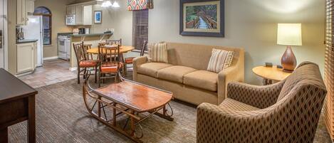 A living room with a sofa, armchair, wooden coffee table, and dining area with chairs and a table.