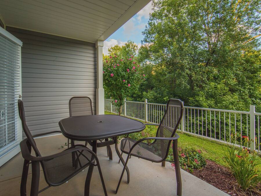 A covered patio with a table and four chairs, a white railing, and a garden with flowering plants.