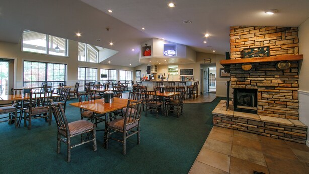 A spacious indoor dining area with multiple tables and chairs, a stone fireplace, and a kitchen area in the background. - Holiday Inn Club Vacations Holiday Hills Resort Branson by IHG (Branson)