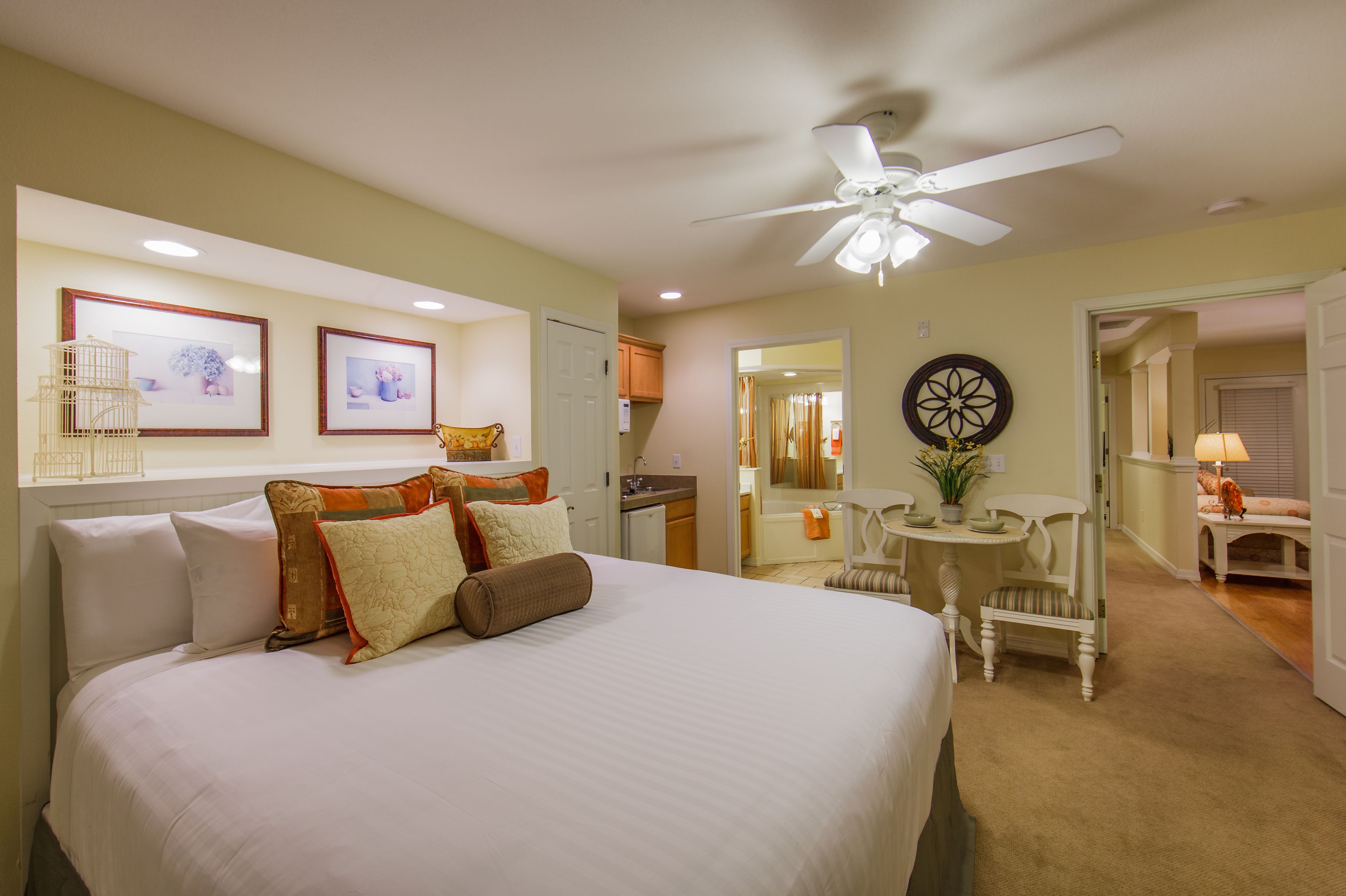 A bedroom with a large bed, a ceiling fan, a small table with a chair, and a bathroom visible through an open door.