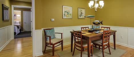 A dining room with a wooden table and chairs, a chandelier, and artwork on the walls.