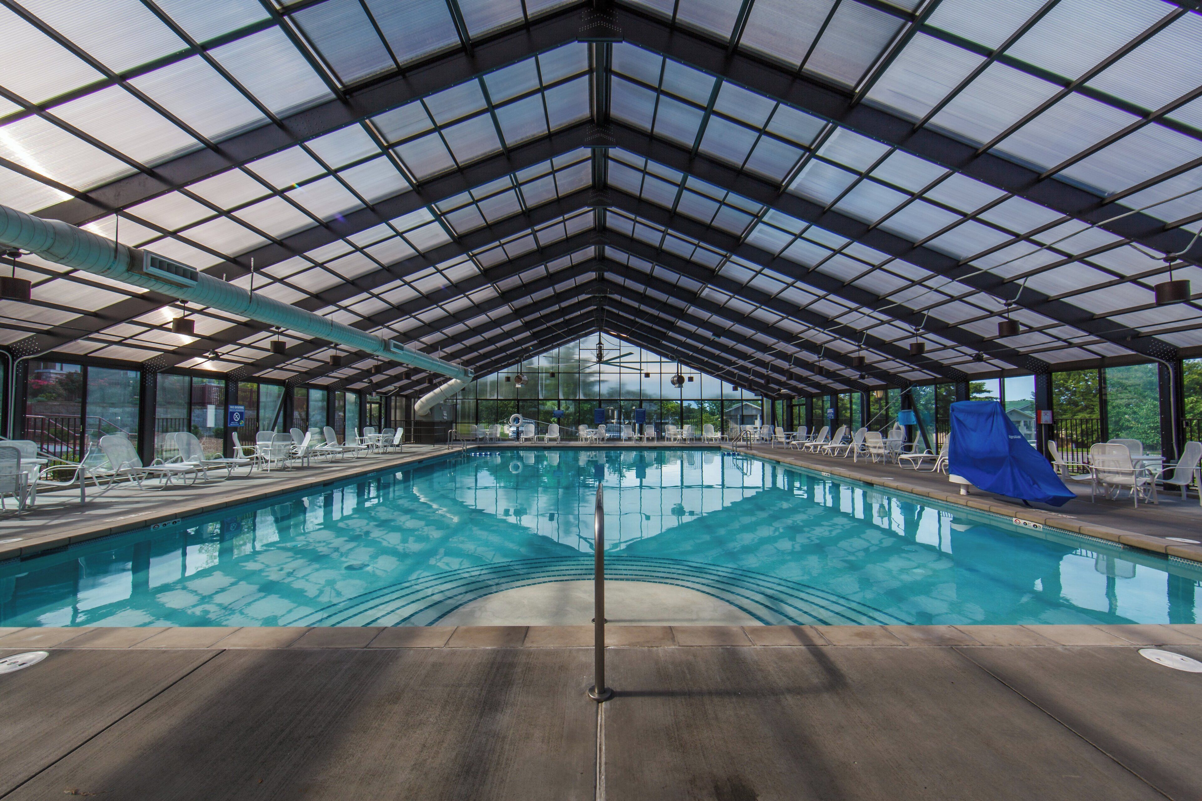 An indoor swimming pool with a glass ceiling, surrounded by lounge chairs and a view of the sky.