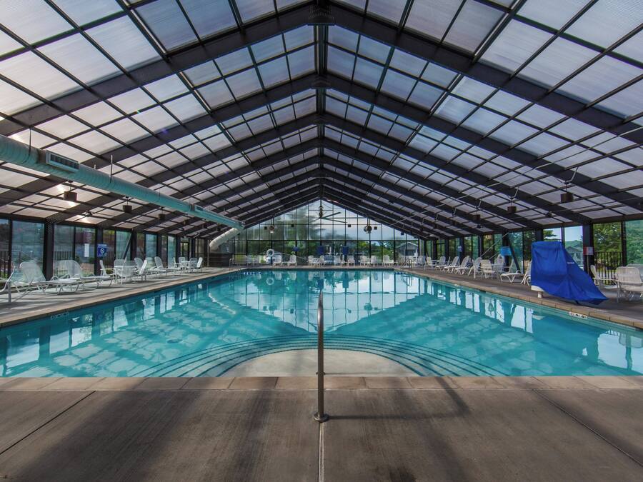 An indoor swimming pool with a glass ceiling, surrounded by lounge chairs and a view of the sky.