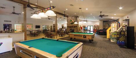 A recreational area with pool tables, ceiling fans, and arcade games.