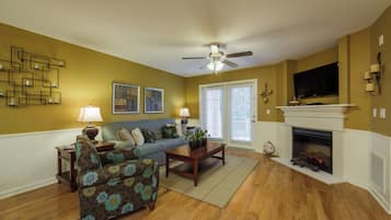 A living room with a sofa, armchairs, a coffee table, a fireplace, and a television.