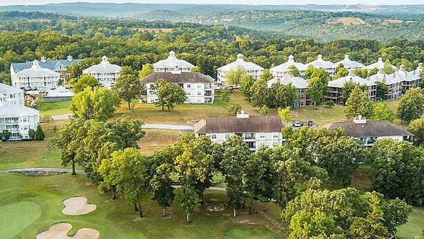 Un hotel grande de varios pisos con un patio central rodeado de árboles y un campo de golf.