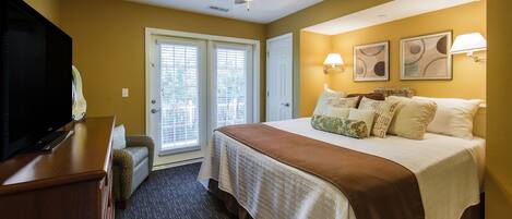 A hotel room with a bed, a television, a ceiling fan, and a door leading to a balcony.