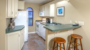 Una cocina con electrodomésticos blancos, encimera verde y taburetes de madera.
