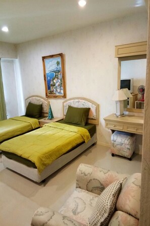 A bedroom with two beds, a bedside table with a lamp, a chair, a desk with a mirror, and a painting on the wall. - Vip Condochain By Kittima (Rayong)