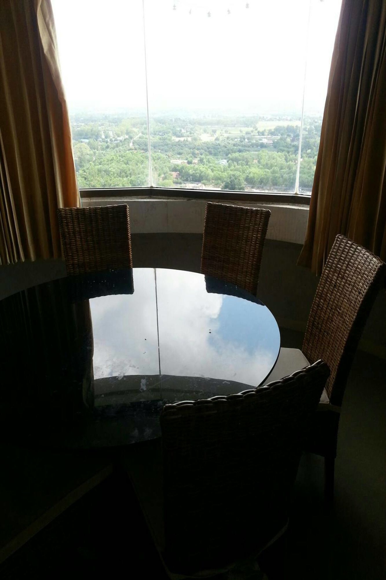 Mesa redonda con cuatro sillas de mimbre en una habitación con un ventanal que ofrece vistas a un paisaje verde.