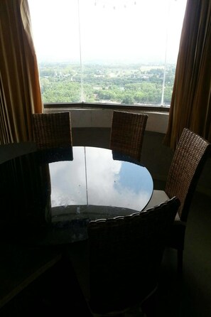 A round table with four wicker chairs in a room with a large window offering a view of a green landscape. - Vip Condochain By Kittima (Rayong)