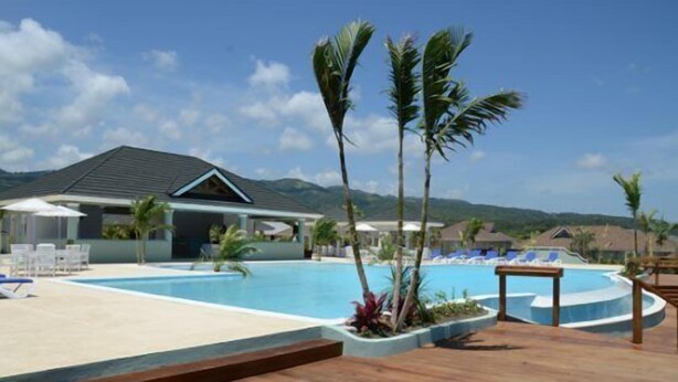 A resort pool area with a wooden deck, lounge chairs, and a building with a sloped roof. - Richmond Estate (St. Ann's Bay)