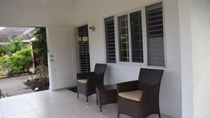 A covered patio area with two wicker chairs and a small table, white tiled flooring, and a door leading outside. - Richmond Estate (St. Ann's Bay)
