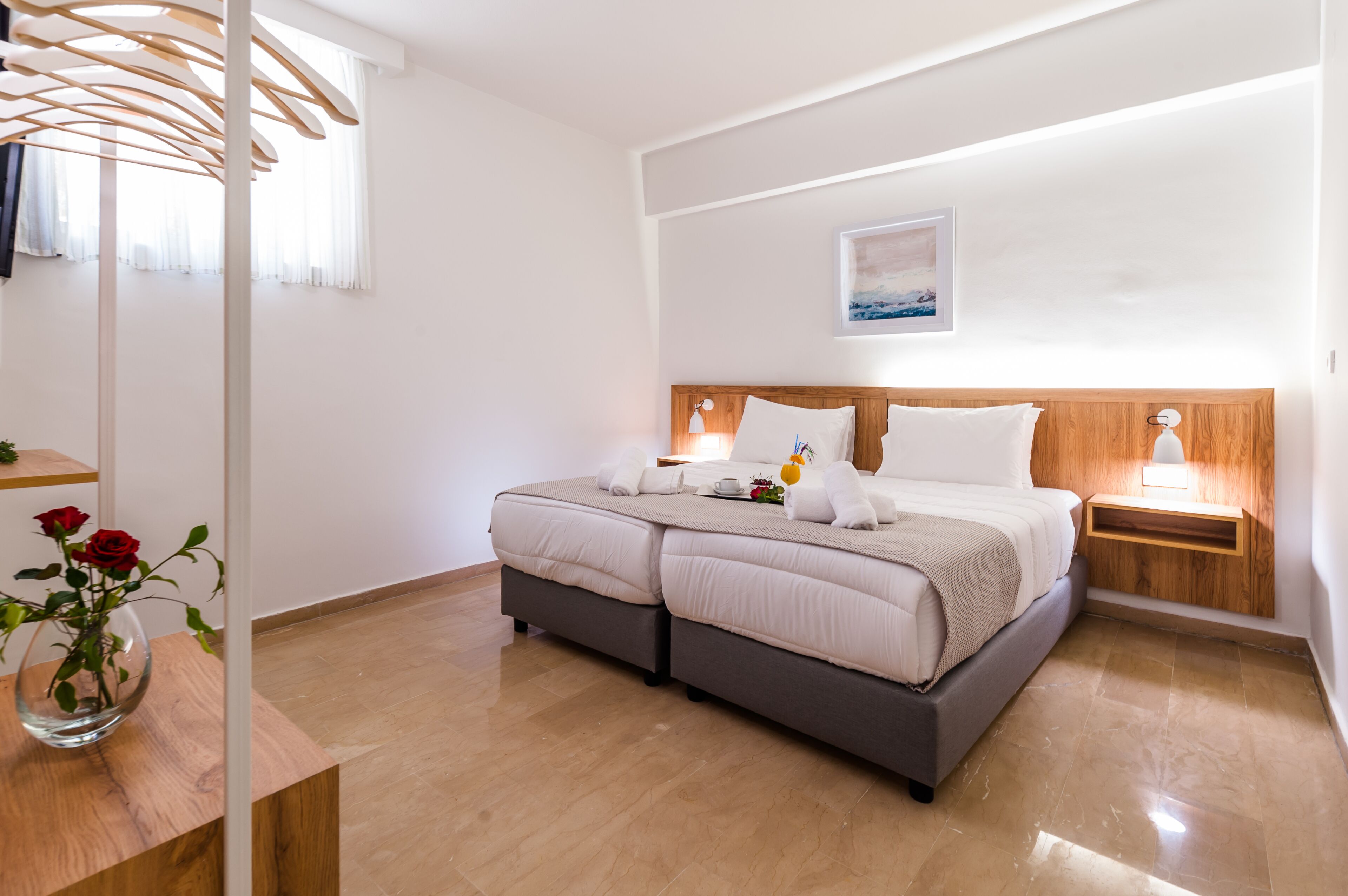 Une chambre moderne avec un grand lit, une tête de lit en bois, une table de chevet avec une lampe et un vase rempli de fleurs.