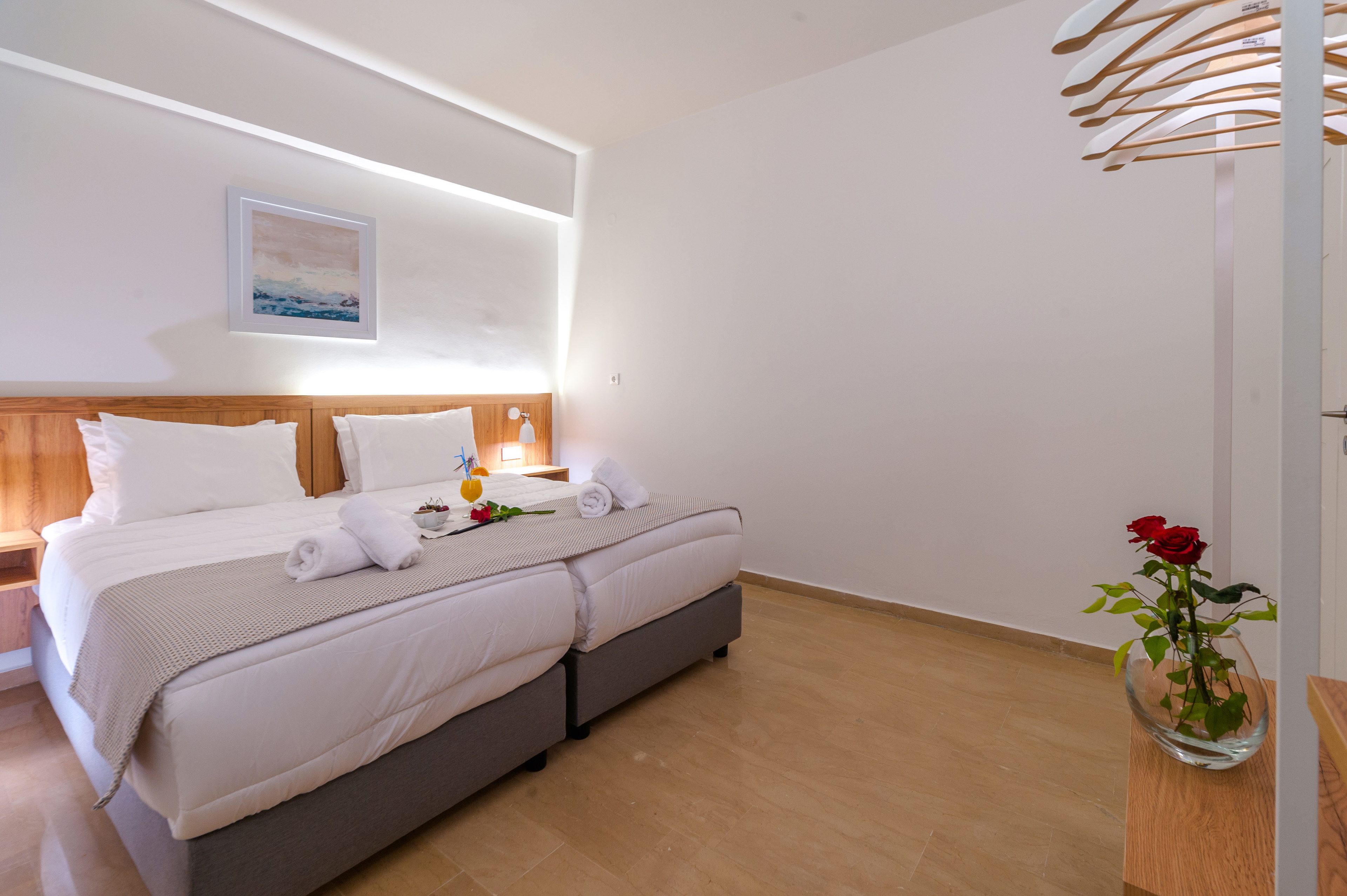 A double bed with a wooden headboard, a bedside table with a lamp, and a vase with a red rose on the right side.
