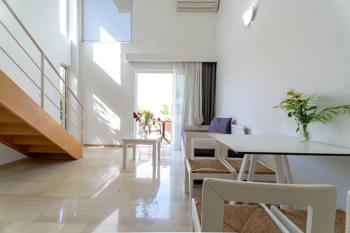 A modern living room with a staircase, a dining area, and a view of the outdoors.