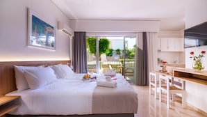 Ein Hotelzimmer mit einem großen Bett, einem Schreibtisch, einem Fernseher und einem Balkon mit Blick auf Bäume und Gebäude.