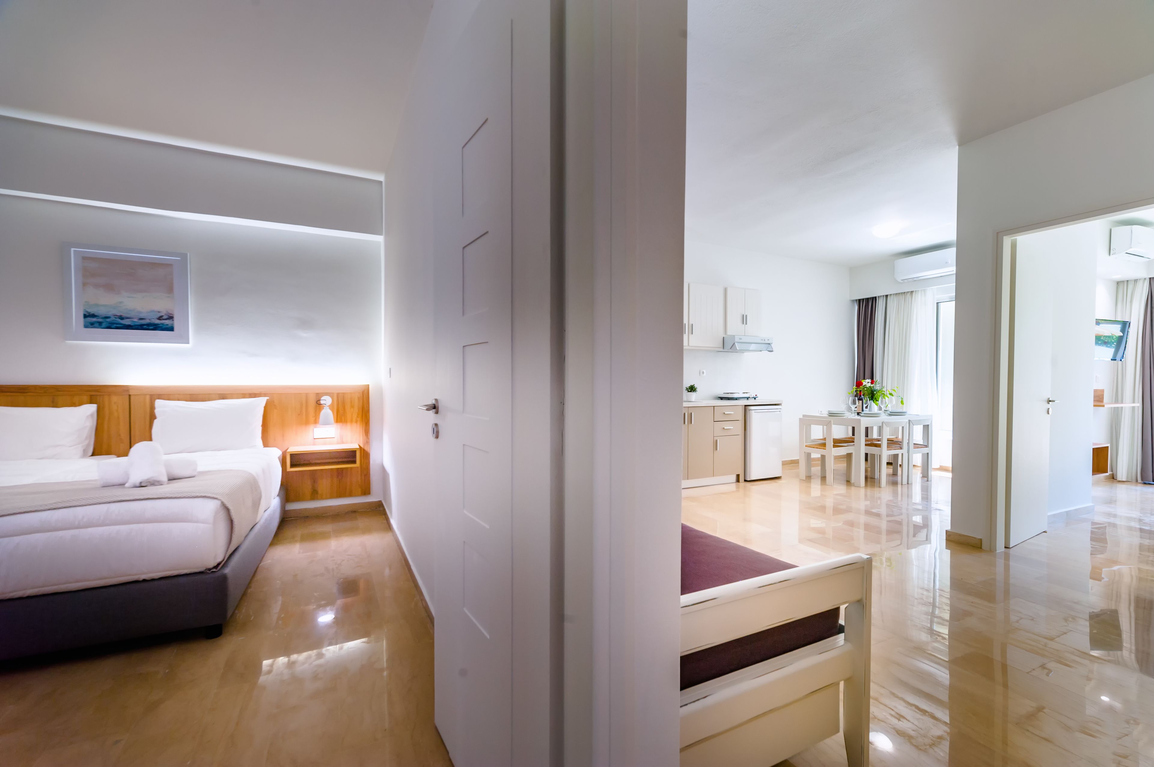 A hotel room with a bed, bedside table, and a view into the adjacent dining area.