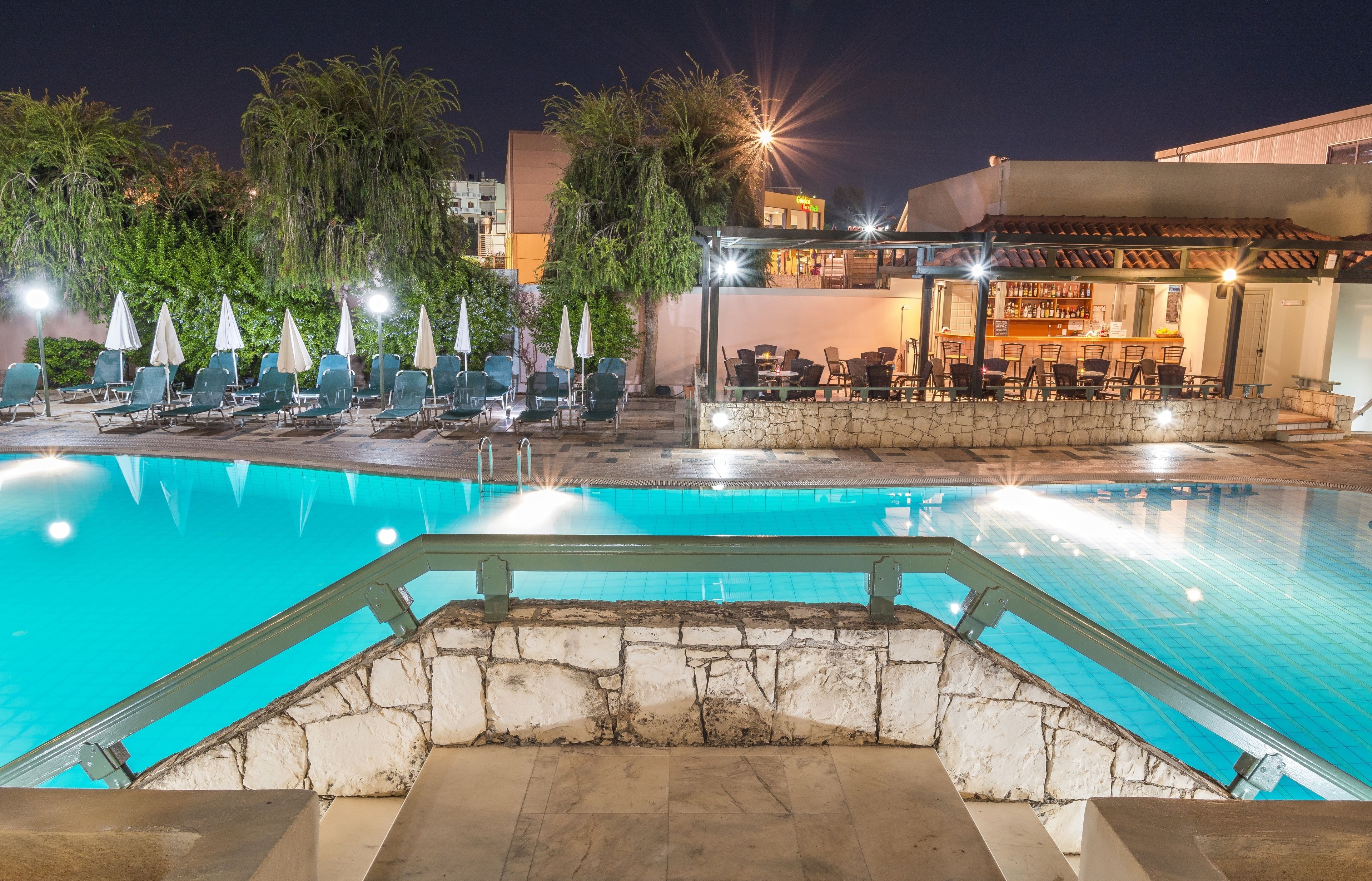 A swimming pool with lounge chairs and umbrellas, a bar area with outdoor seating, and a stone wall.