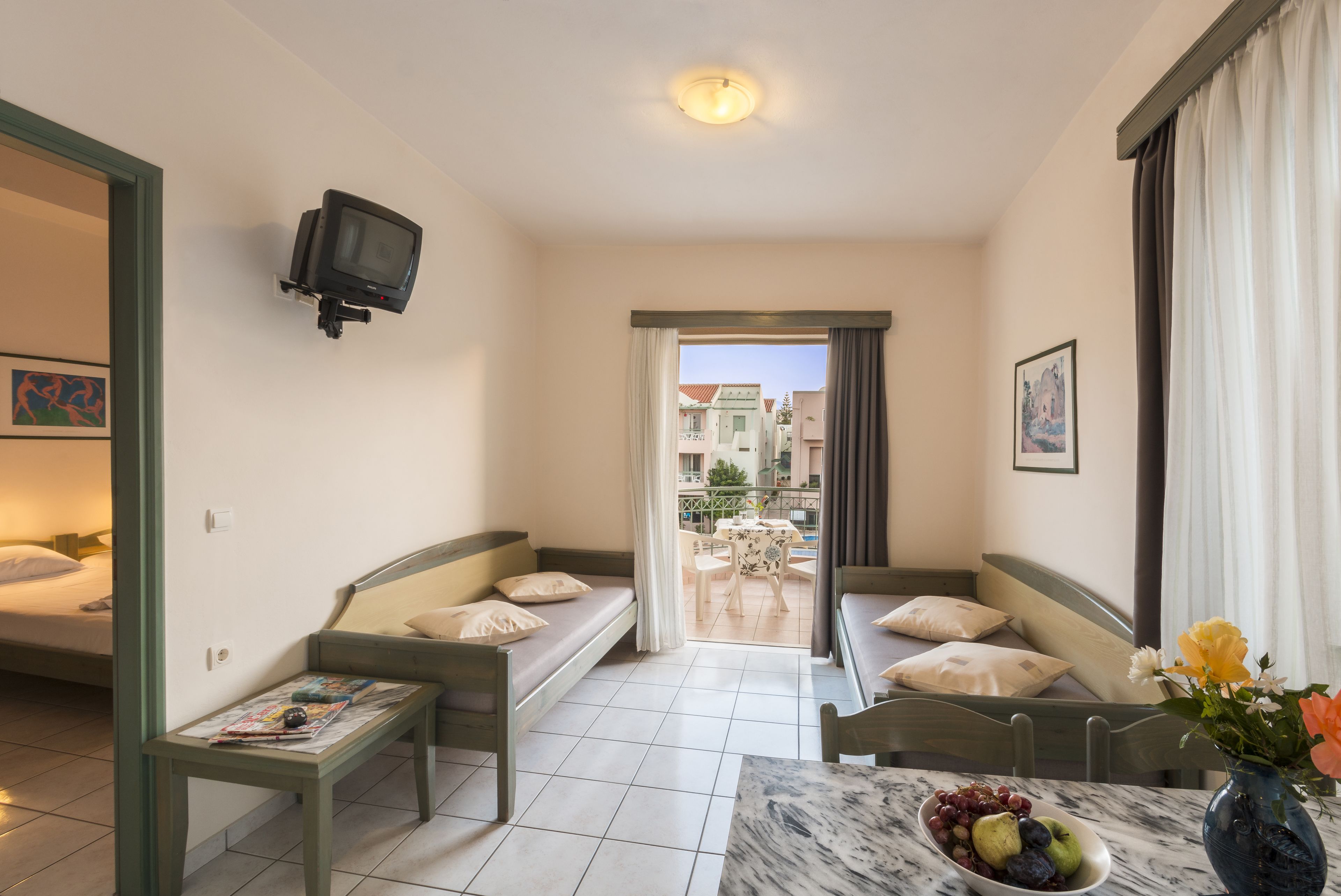 Une chambre d’hôtel compacte comprenant un canapé-lit, une petite table, un téléviseur fixé au mur et un balcon offrant une vue sur les bâtiments.